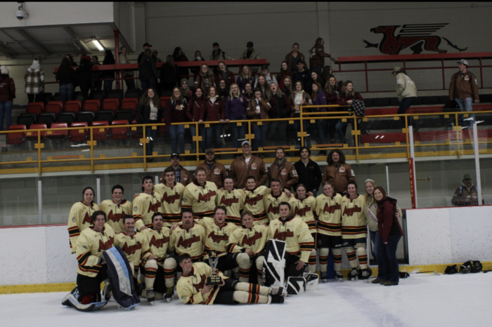 A group photo of the Aggies hockey team posing on the ice rink in their yellow hockey uniforms.
